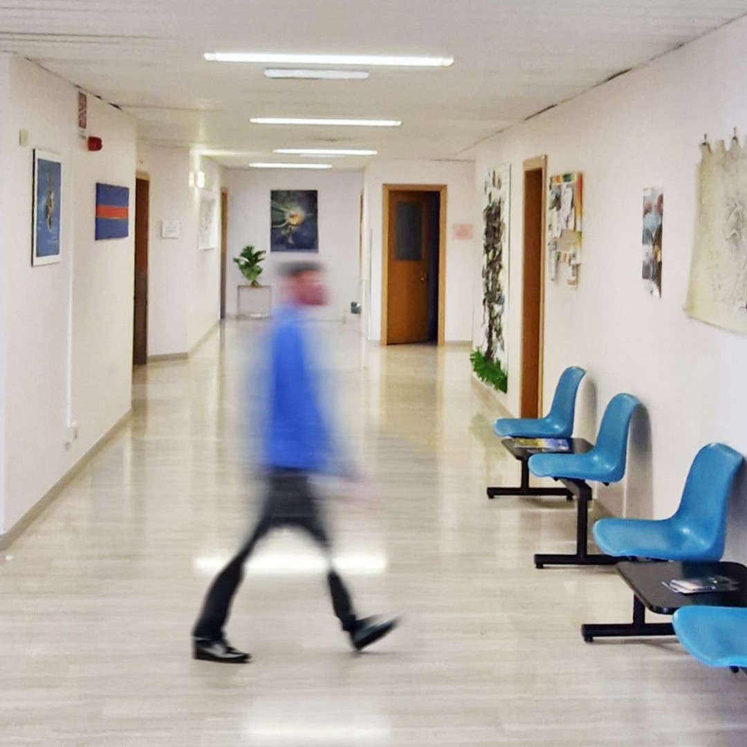 Una persona poco visibile attraversa un corridoio su cui si affacciano diverse porte